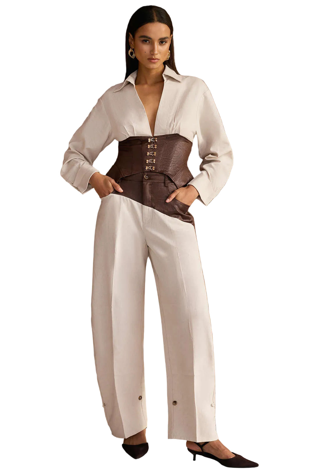 Woman wearing a white blouse with a brown corset and white pants against a wooden paneled wall.