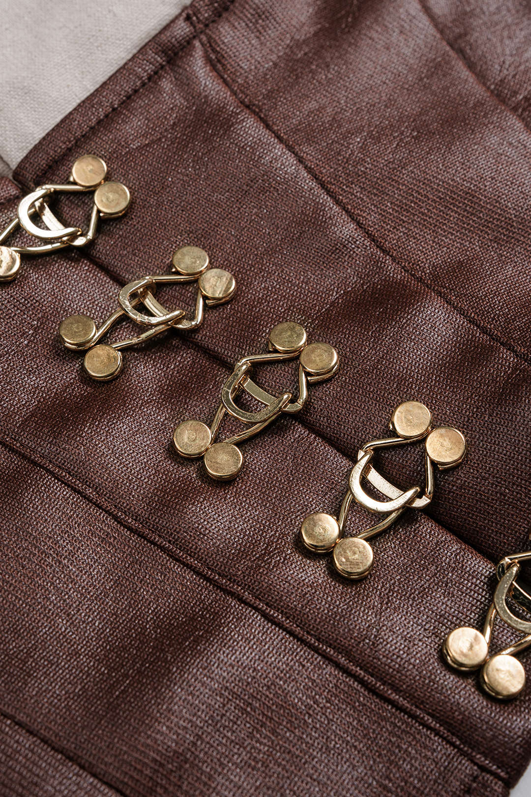 Close-up of a brown fabric with gold buttons on a gray background