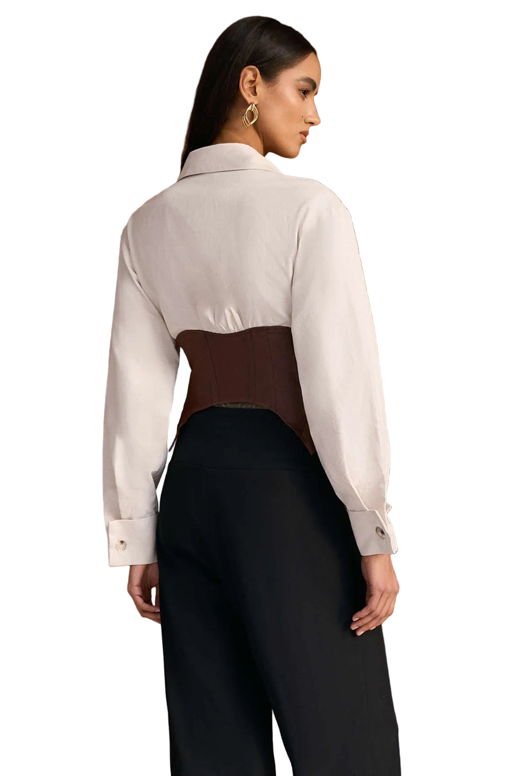 Woman wearing a white shirt with a brown accent and black pants against a wooden wall.