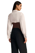 Woman wearing a white shirt with a brown accent and black pants against a wooden wall.